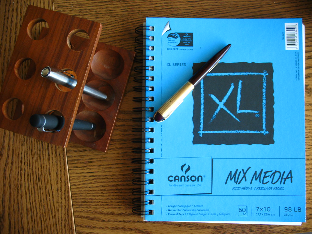 A notebook and fountain pens arranged on a wooden desk